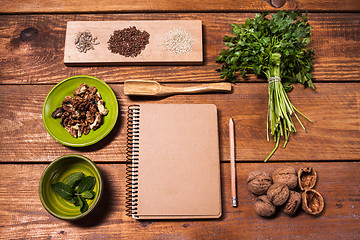 Image showing Notebook for recipes, walnuts, parsley and seeds on wooden table.