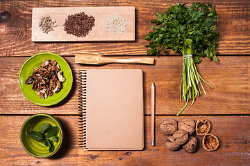 Image showing Notebook for recipes, walnuts, parsley and seeds on wooden table.