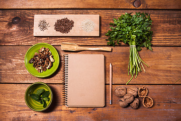 Image showing Notebook for recipes, walnuts, parsley and seeds on wooden table.