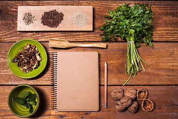 Image showing Notebook for recipes, walnuts, parsley and seeds on wooden table.