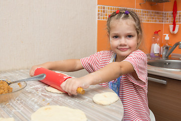 Image showing The girl rolls the dough with a rolling pin pancake for pies and looks in the picture