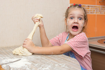 Image showing The girl tears off a piece of dough for pies and happily looks into the frame