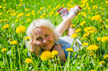 Image showing A woman lies in a clearing and sniffs a flower  