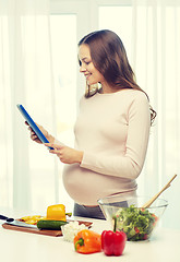 Image showing happy pregnant woman with tablet pc cooking food