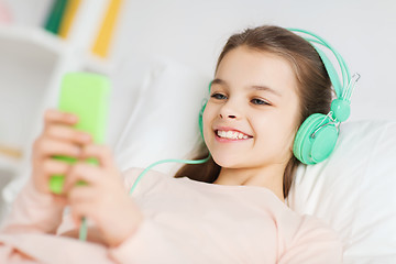 Image showing happy girl lying in bed with smartphone at home