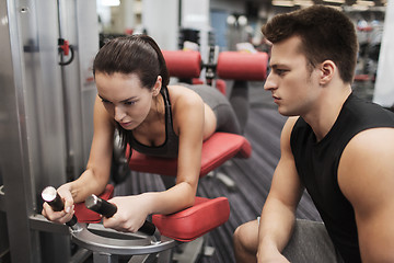 Image showing young woman with trainer exercising on gym machine