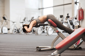 Image showing young woman flexing back muscles on bench in gym