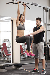 Image showing young woman with trainer doing leg raises in gym