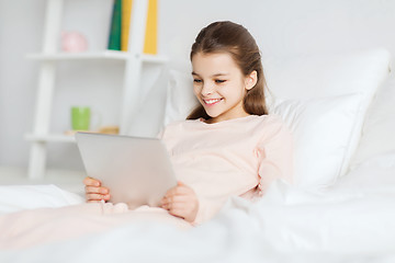 Image showing happy girl lying in bed with tablet pc at home