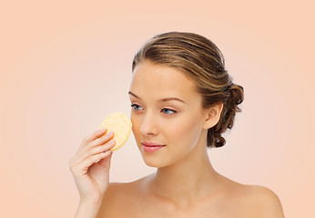 Image showing young woman cleaning face with exfoliating sponge