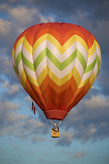 Image showing Orange and yellow hot-air balloon floating among clouds