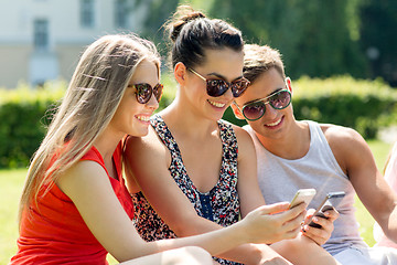 Image showing smiling friends with smartphones sitting in park