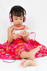 Image showing Chinese little girl on headphones holding mobile phone