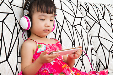 Image showing Chinese little girl on headphones holding mobile phone