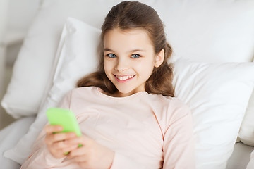 Image showing happy girl lying in bed with smartphone at home