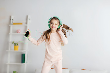 Image showing girl jumping on bed with smartphone and headphones