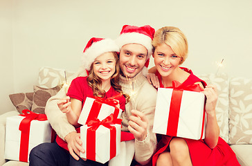 Image showing smiling family holding gift boxes and sparkles