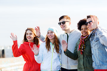 Image showing happy teenage friends waving hands on city street