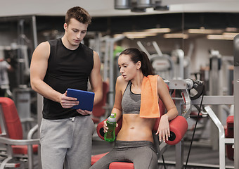 Image showing smiling young woman with personal trainer in gym