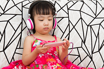 Image showing Chinese little girl on headphones holding mobile phone