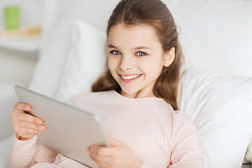 Image showing happy girl lying in bed with tablet pc at home