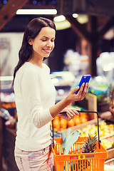 Image showing happy woman with basket and smartphone in market