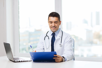 Image showing happy doctor with clipboard and laptop in office