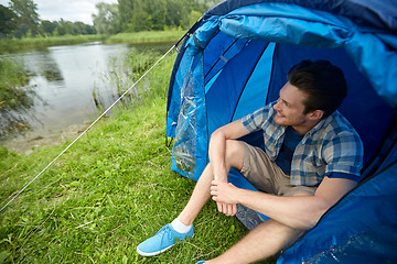 Image showing happy young man sitting in tent at camping