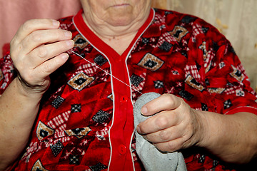 Image showing Old woman to sew over a tear