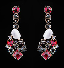 Image showing earring with colorful red gems on black background