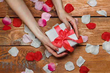 Image showing Valentines Day gift and Female hands on wooden background with petals