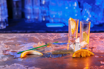 Image showing The spilled cocktails with ice cubes on blue color in the bar