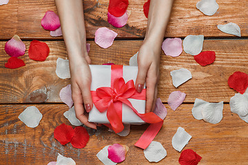 Image showing Valentines Day gift and Female hands on wooden background with petals