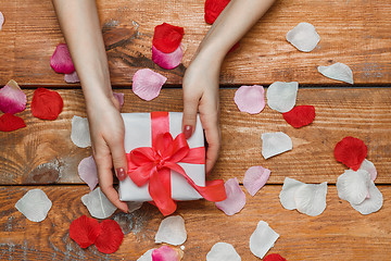 Image showing Valentines Day gift and Female hands on wooden background with petals