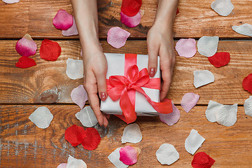 Image showing Valentines Day gift and Female hands on wooden background with petals
