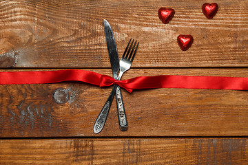 Image showing The red ribbon, fork and knife on wooden background