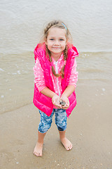 Image showing Three year old girl standing on the beach with shells in hand