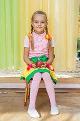 Image showing Girl sitting on a chair with an apple in his hand on a matinee in kindergarten