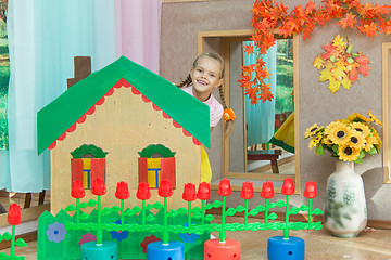 Image showing The girl looks out from behind the scenery a country house in the matinee in kindergarten