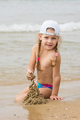 Image showing  The three-year girl builds a sand castle on the beach