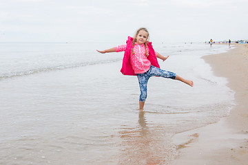 Image showing Three year old girl having fun stood on one leg on the beach