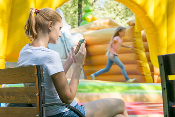 Image showing Young mother with a child at the phone waiting inflatable trampolines