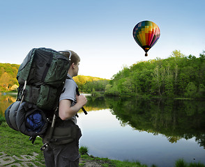 Image showing Backpacking hiker encounters a hot air balloon floating above a 