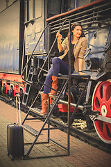 Image showing pretty middle-aged woman with luggage near the old steam locomot