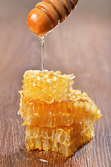 Image showing Honey dripping on honeycombs on wooden background