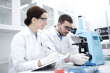 Image showing scientists with clipboard and microscope in lab