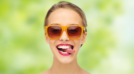 Image showing happy young woman in sunglasses showing tongue