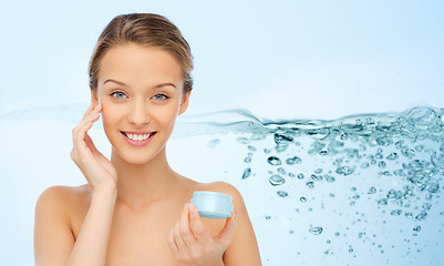 Image showing smiling young woman applying cream to her face