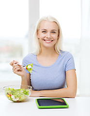 Image showing smiling woman eating salad with tablet pc at home