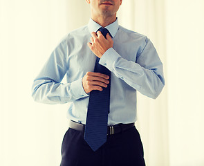 Image showing close up of man in shirt adjusting tie on neck